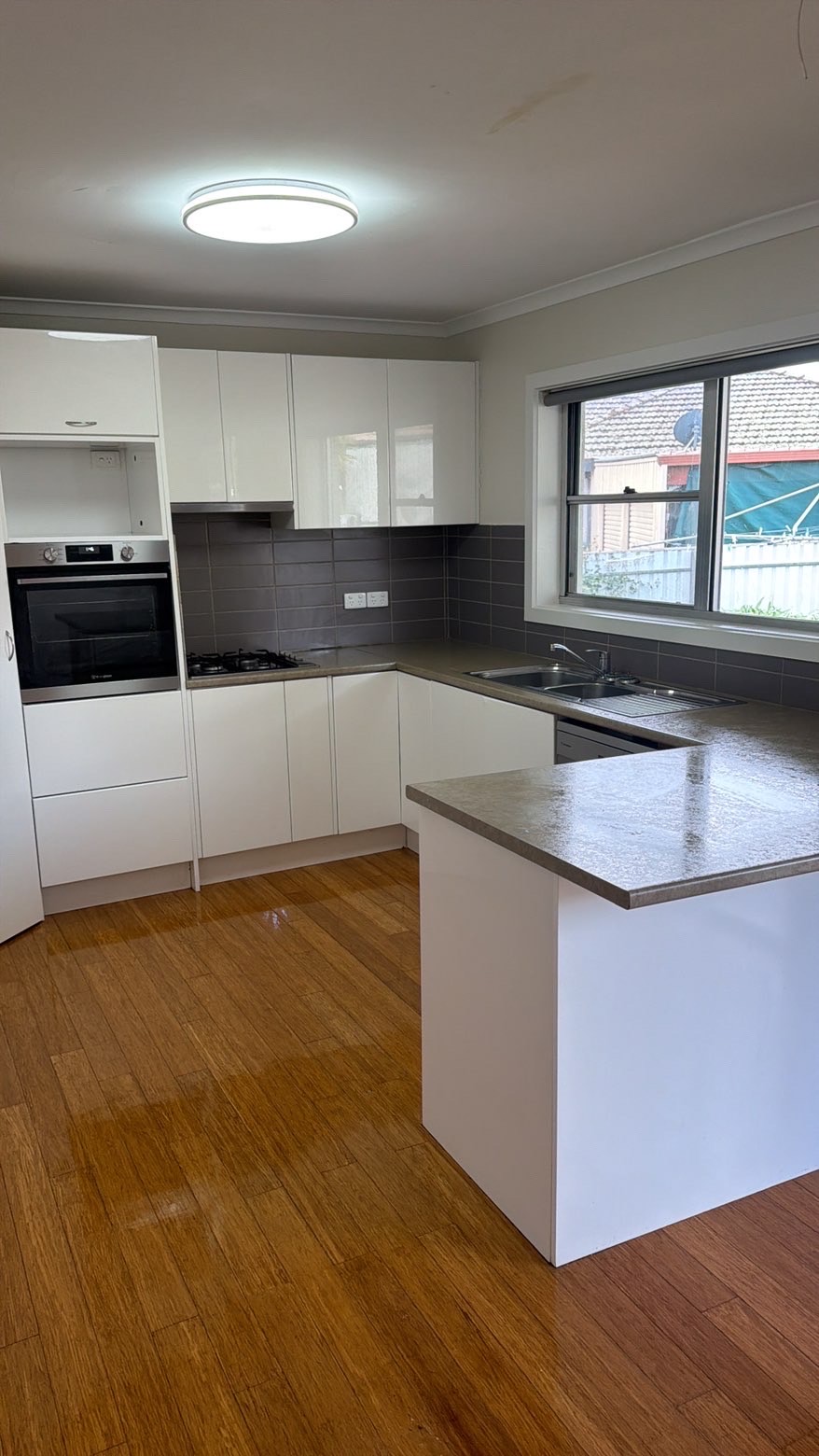 A freshly cleaned kitchen with spotless white cabinetry, polished benchtops and gleaming timber floors.